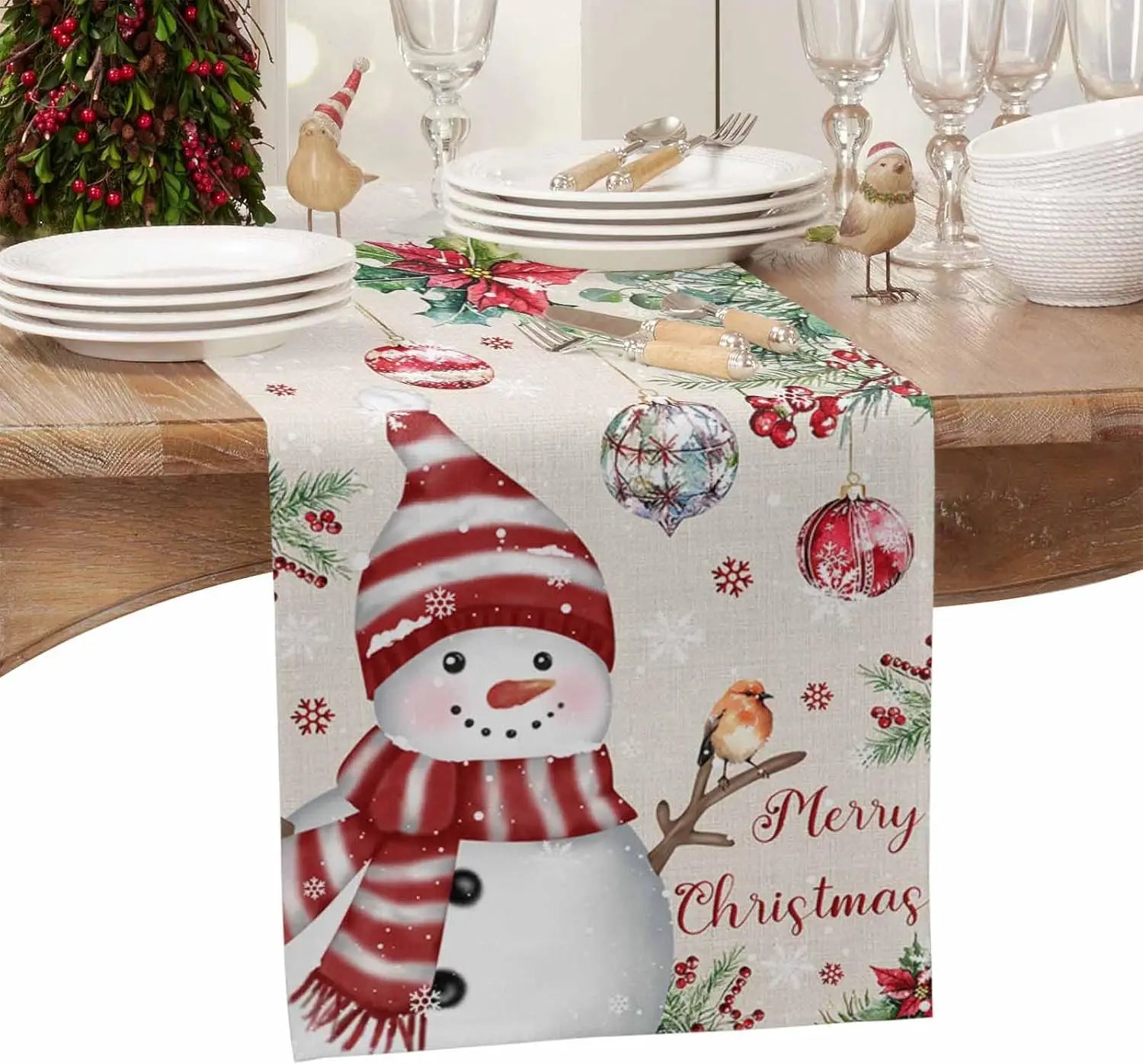 Un décor de table de Noël avec des plats, des verres et un chemin de table orné de motifs de Noël, notamment un bonhomme de neige et des boules de Noël.