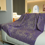 Couverture à motif violets et gris posée sur un canapé dans un salon.