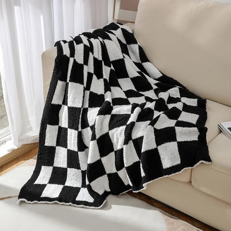 Couverture en polaire blanche et noire à motifs géométriques carrés, posée sur un canapé, créant une ambiance cosy et graphique dans la pièce.