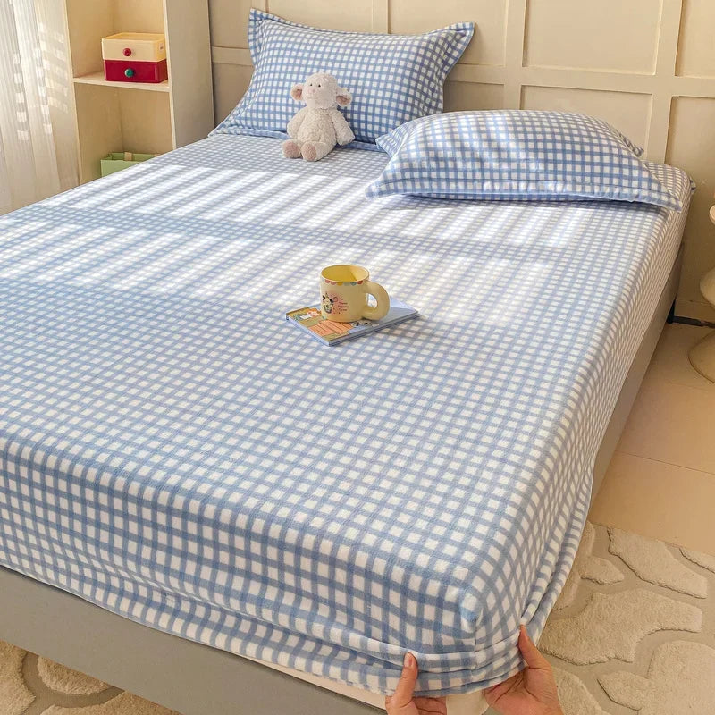 Une chambre à coucher mignonne et douillette avec des draps à carreaux bleus et blancs, un ours en peluche et une tasse posée sur le lit.