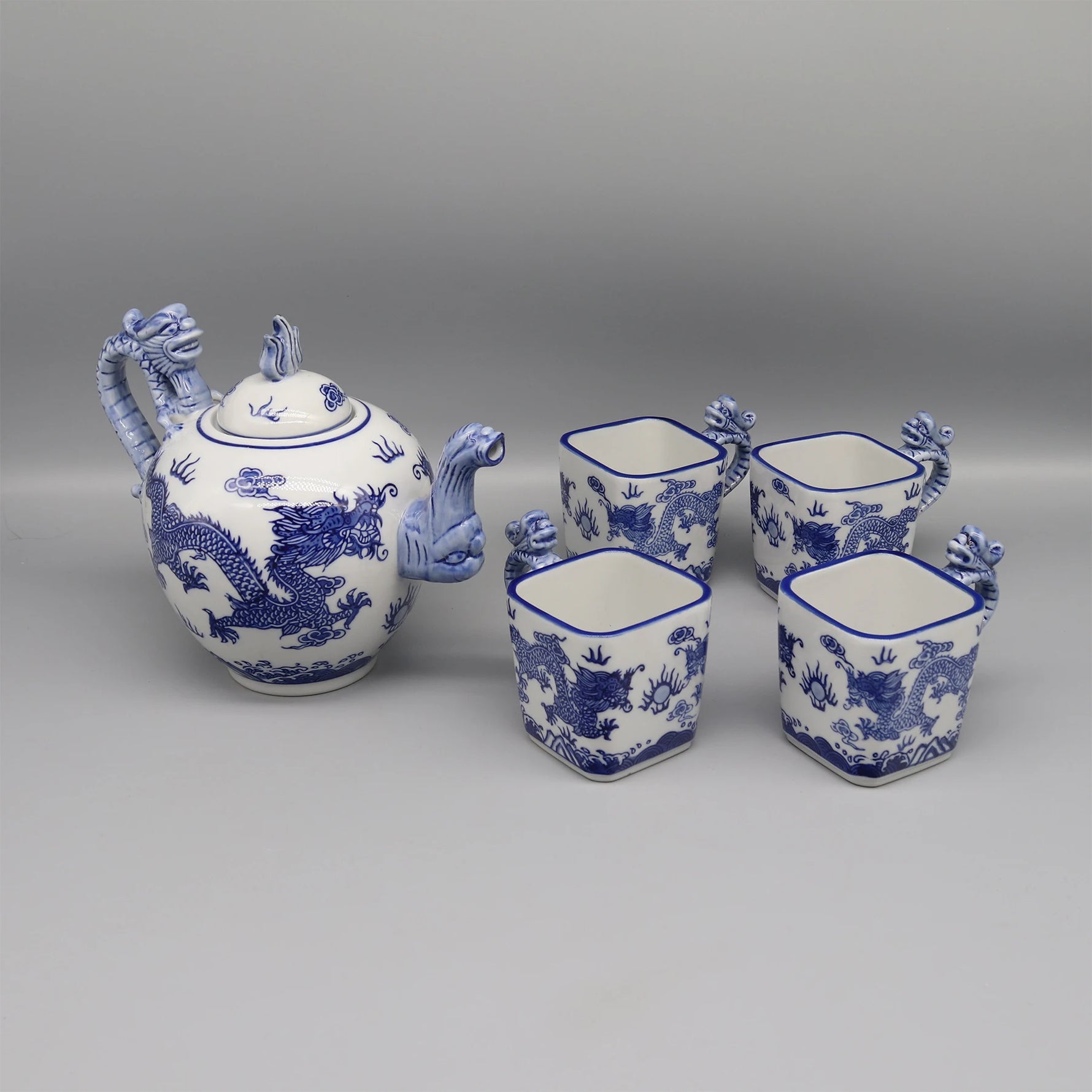 Série de pièces de porcelaine bleue et blanche ornées de motifs de dragons, comprenant une théière, deux tasses et une cafetière.