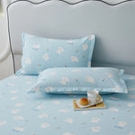 Parure de lit bleue ciel avec motifs de chiots imprimés, composée d'un oreiller et d'un couvre-lit, posée sur un lit avec un plateau contenant une tasse et des macarons.