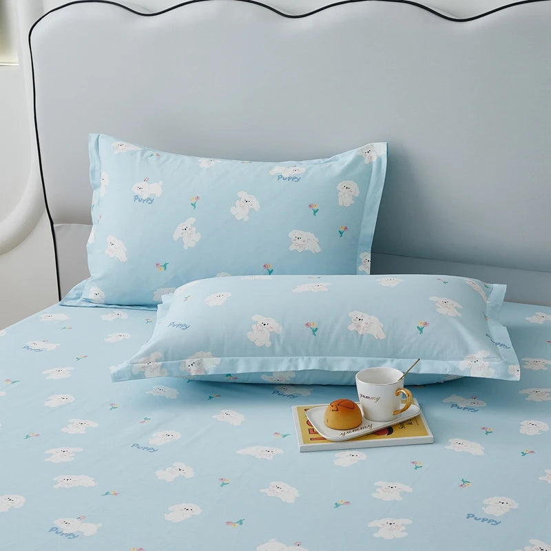 Parure de lit bleue ciel avec motifs de chiots imprimés, composée d'un oreiller et d'un couvre-lit, posée sur un lit avec un plateau contenant une tasse et des macarons.