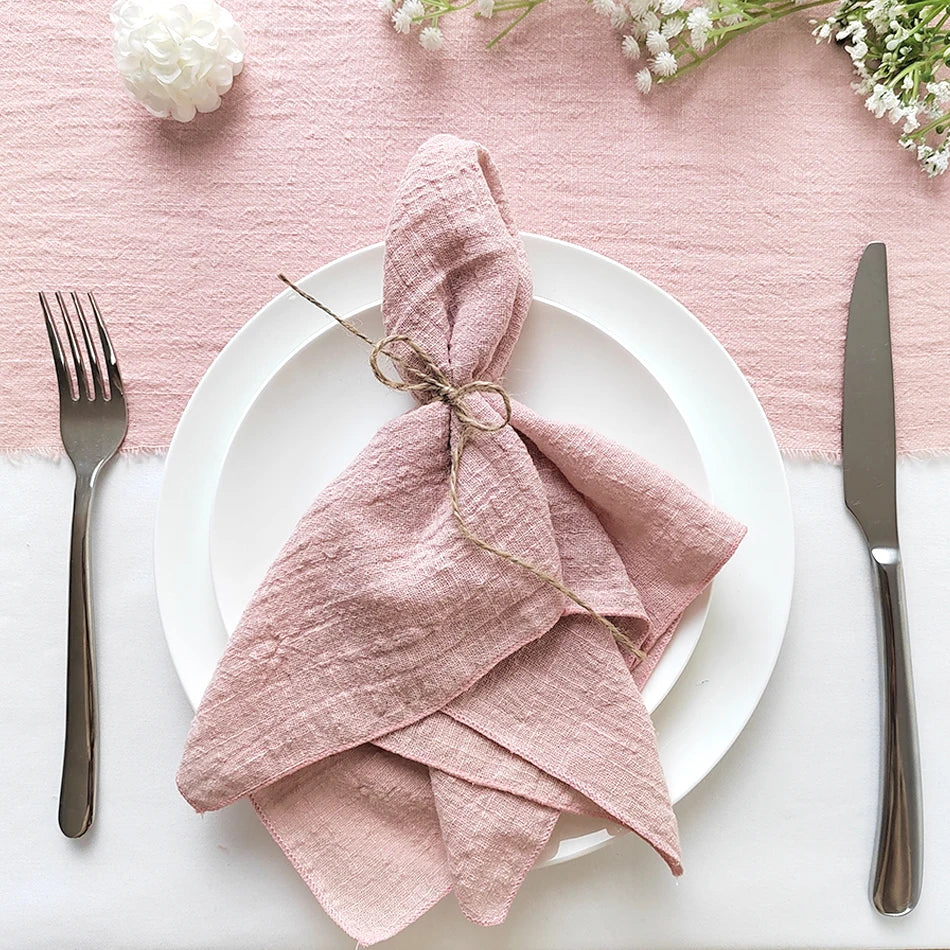 Une élégante table de service avec des accents de rose pâle, une nappe texturée nouée avec un lacet, accompagnée d'un couvert en métal sombre, créant une ambiance raffinée et invitante.