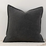 Coussin décoratif gris foncé avec bordure sombre, posé sur un sol clair.