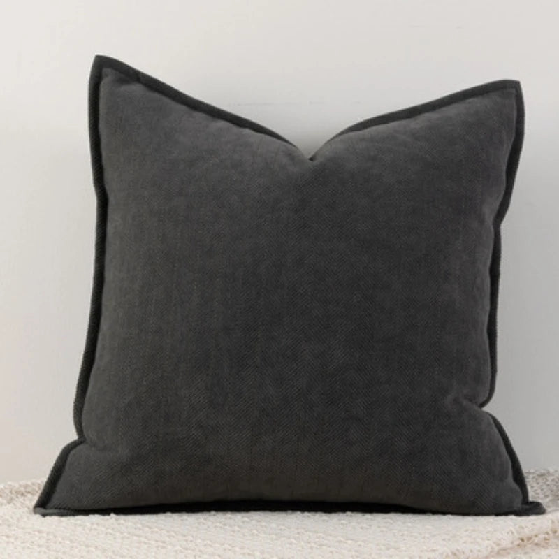 Coussin décoratif gris foncé avec bordure sombre, posé sur un sol clair.