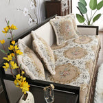 Un canapé confortable avec des coussins ornés de motifs floraux et de bordures dorées, placé dans un intérieur élégant et décoré avec des plantes.