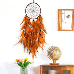 Un magnifique attrapeur de rêves orange aux plumes élégantes, suspendu au mur avec un miroir et un globe terrestre, créant une atmosphère apaisante et méditative.