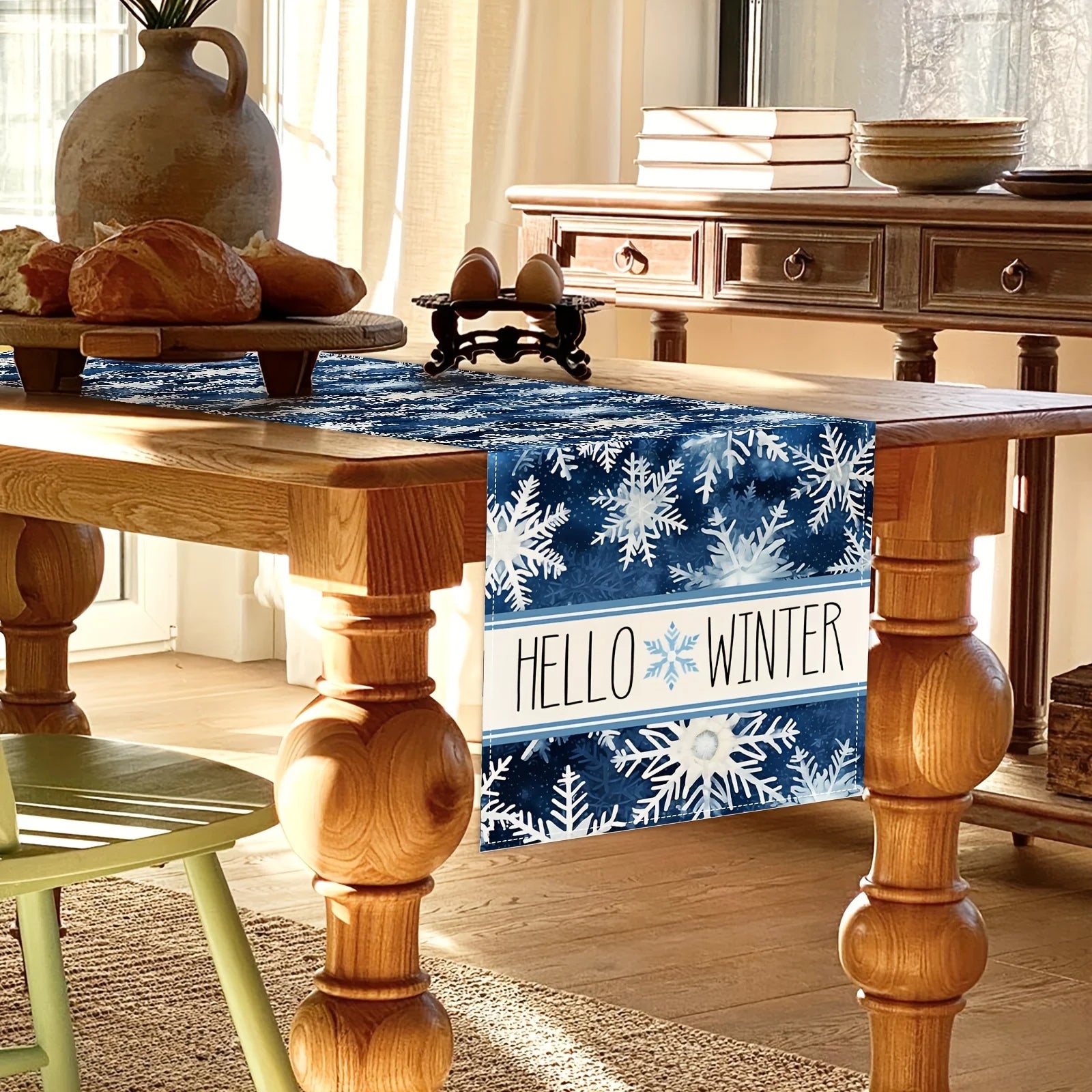 Une table en bois rustique avec des décorations hivernales, notamment un chemin de table bleu foncé avec des flocons de neige blancs, des pains artisanaux et des ustensiles de cuisine vintage, créant une ambiance chaleureuse et accueillante pour la saison froide.