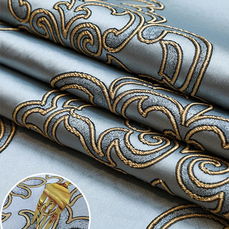 Motif brodé abstrait avec des formes organiques de couleurs grise et dorée sur un tissu bleuâtre, créant un élégant design décoratif.