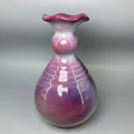 Un élégant vase en verre soufflé aux nuances de rose et de violet, avec des motifs ondulants et des points lumineux créant un effet irisé captivant.