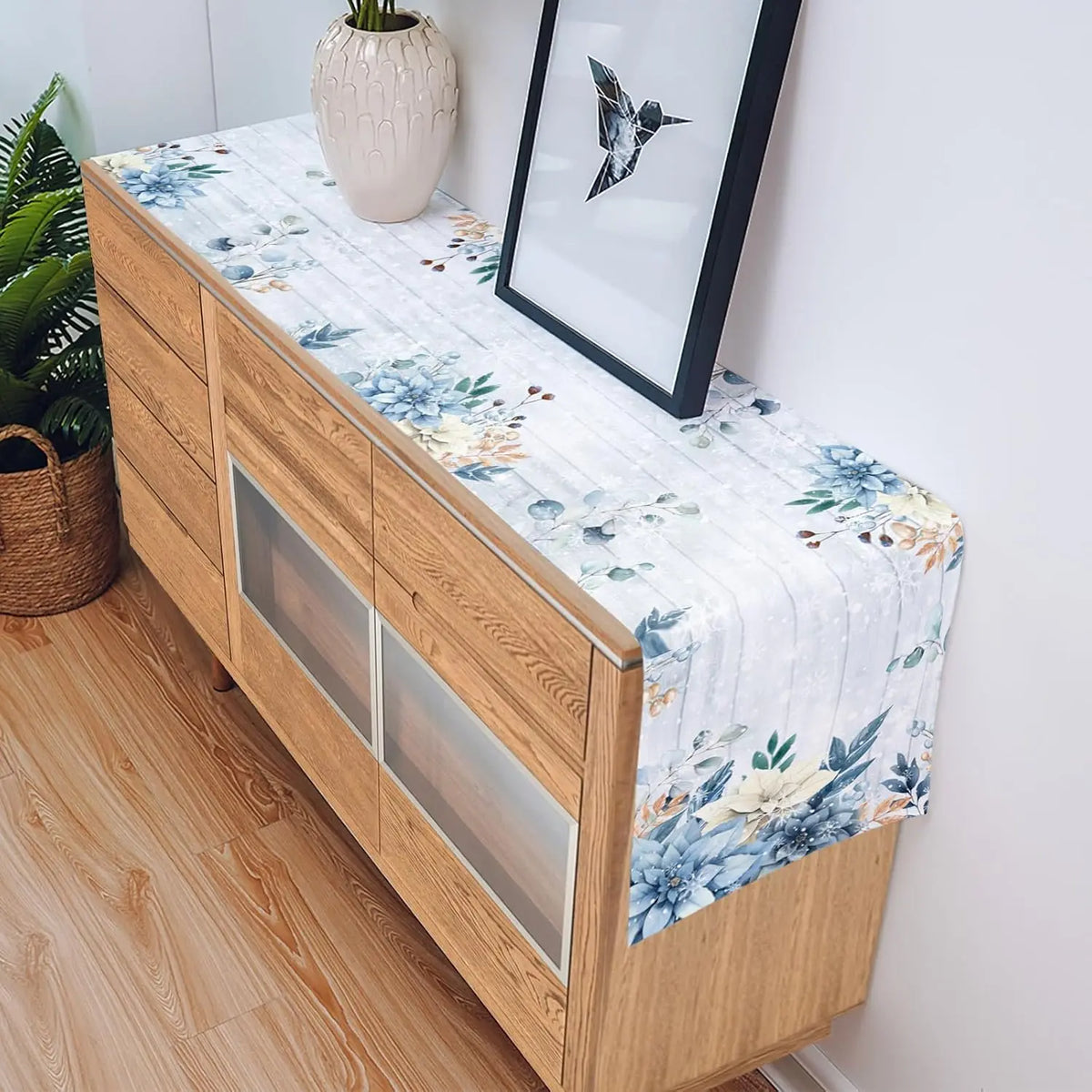 Meuble de rangement en bois avec des motifs floraux sur le dessus, décoré d'un vase beige et d'un cadre mural avec un motif d'oiseau.