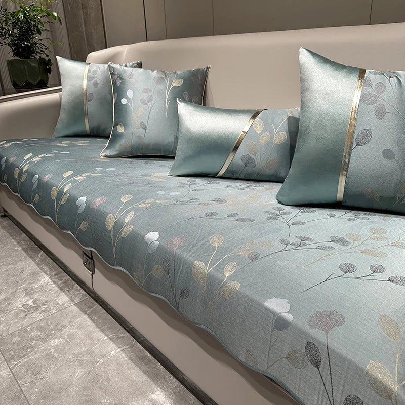 Couette en satin avec motifs floraux gris et dorés, comprenant des oreillers assortis disposés sur un grand canapé.