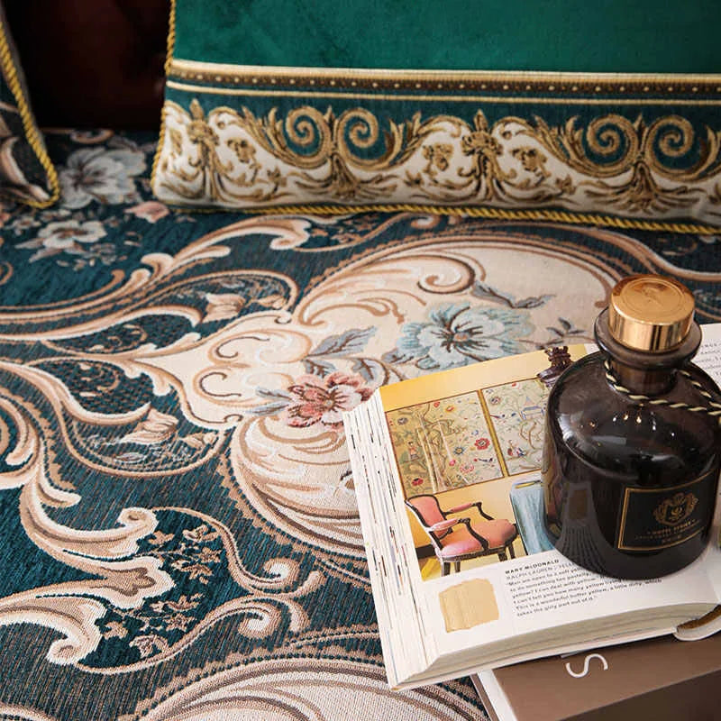 L'image montre une table élégante avec un tapis vert et or décoré de motifs floraux et classiques, sur laquelle reposent un livre et un flacon de parfum de luxe, créant une atmosphère raffinée et sophistiquée.