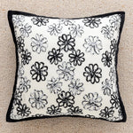 Coussin décoratif avec motif floral noir et blanc sur fond blanc, avec bordure noire.