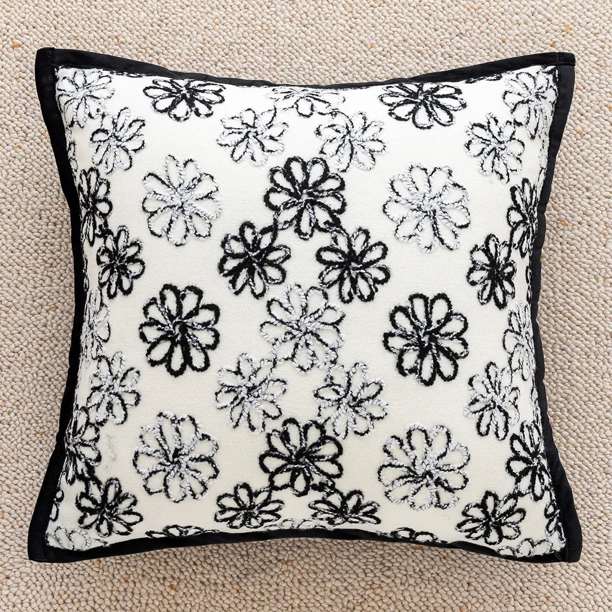 Coussin décoratif avec motif floral noir et blanc sur fond blanc, avec bordure noire.