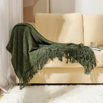 Une couverture verte texturée avec des franges décorative et élégante, reposant sur un canapé beige dans un intérieur confortable.