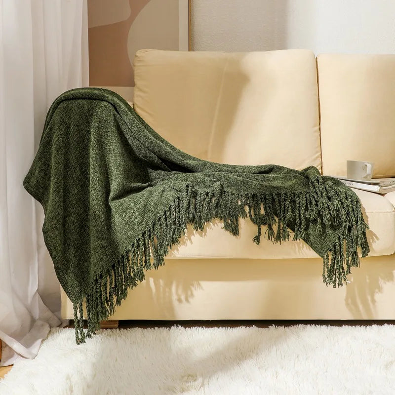 Une couverture verte texturée avec des franges décorative et élégante, reposant sur un canapé beige dans un intérieur confortable.