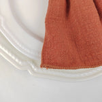 Gros plan sur une serviette de table en étoffe de couleur orange terracotta posée sur un plat transparent.