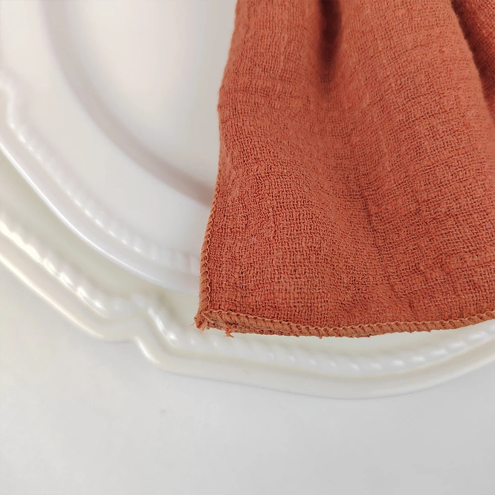 Gros plan sur une serviette de table en étoffe de couleur orange terracotta posée sur un plat transparent.