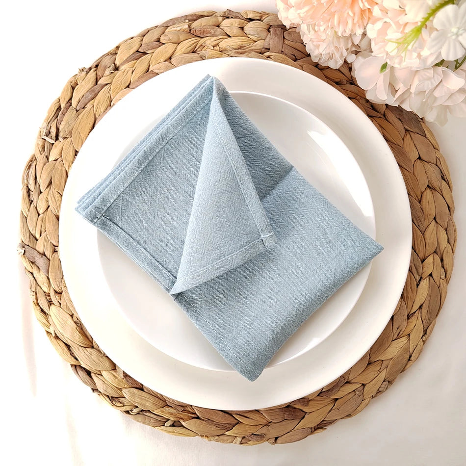 Serviette grise en tissu sur une assiette blanche posée sur un tapis en fibres tressées.