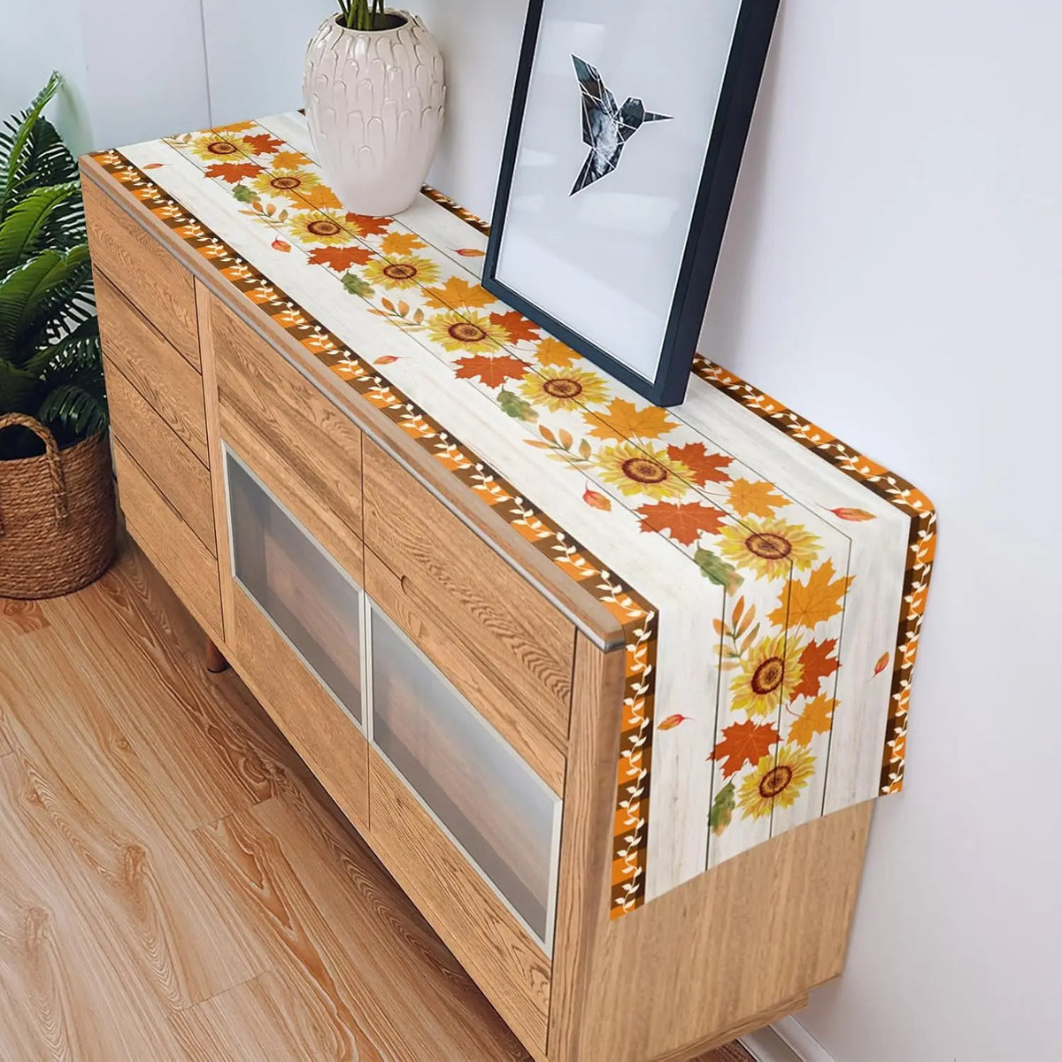 Un meuble en bois avec un chemin de table fleuri, décoré d'un cadre photo et d'une plante en pot.