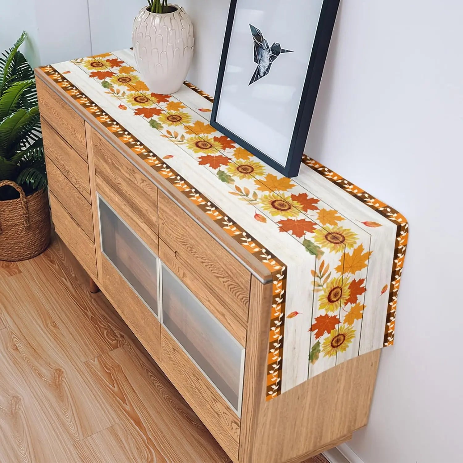 Un meuble en bois avec un chemin de table fleuri, décoré d'un cadre photo et d'une plante en pot.