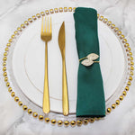 Un élégant service de table composé de couverts dorés et d'un nœud de serviette orné de cristaux brillants sur un fond de marbre blanc.