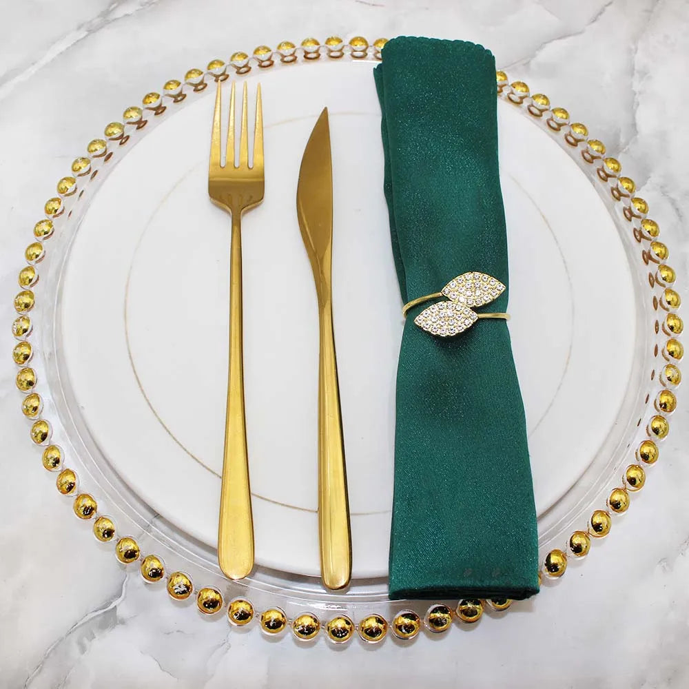 Un élégant service de table composé de couverts dorés et d'un nœud de serviette orné de cristaux brillants sur un fond de marbre blanc.