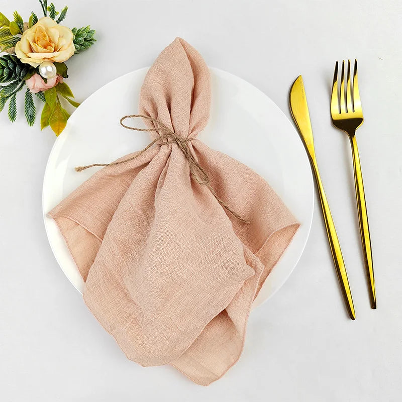 Une belle nappe de table beige, élégamment pliée, posée sur une assiette blanche avec des couverts dorés et une décoration florale.