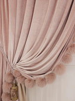 Rideau rose poudré attaché sur le côté avec embrasse, orné de pompons au bas pour une finition élégante et romantique.