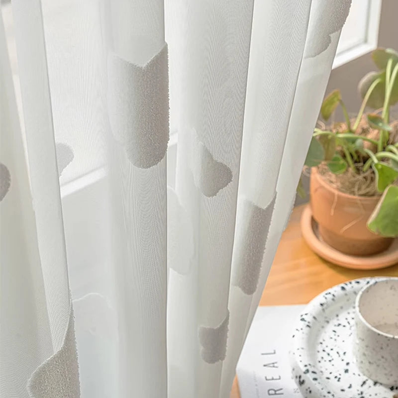 Gros plan sur un voilage blanc décoré de nuages en relief, laissant passer la lumière tout en créant une ambiance douce.