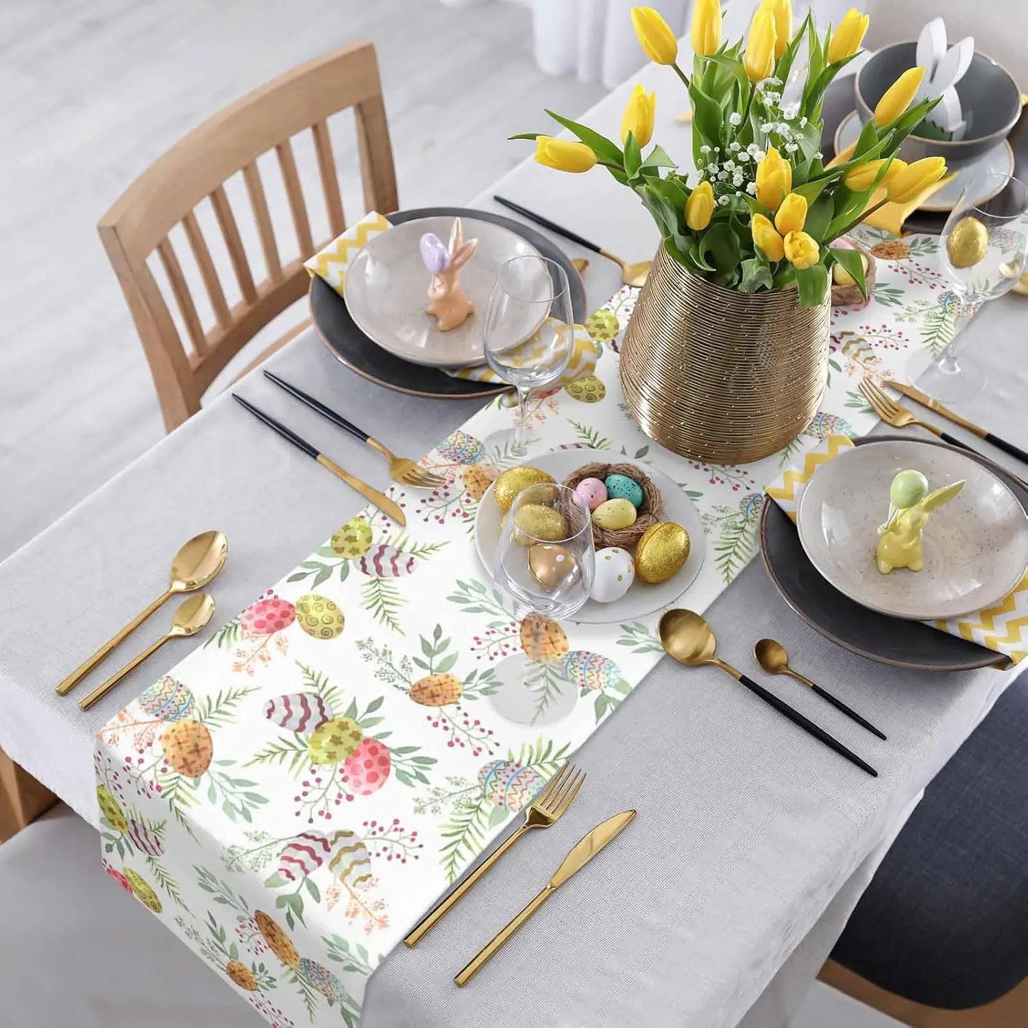 Cette image montre une table de Pâques joliment décorée, avec des fleurs de printemps jaunes, des œufs de Pâques colorés et une belle vaisselle noire et dorée, créant une ambiance festive et printanière.