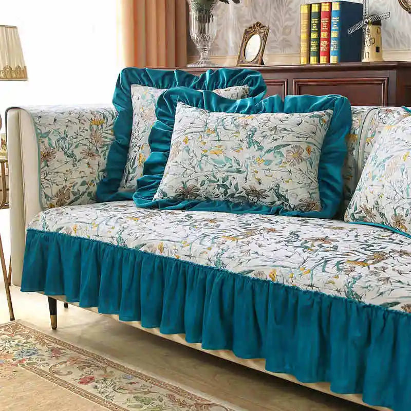 Un canapé recouvert d'un motif floral coloré et harmonieux, avec des coussins assortis et une jupe en velours bleu turquoise, créant une atmosphère chaleureuse et raffinée dans un intérieur élégant.