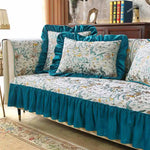 Un canapé recouvert d'un motif floral coloré et harmonieux, avec des coussins assortis et une jupe en velours bleu turquoise, créant une atmosphère chaleureuse et raffinée dans un intérieur élégant.