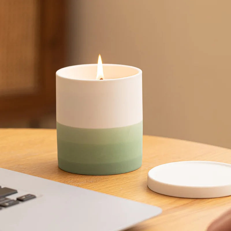 Bougie blanche et verte allumée posée sur un bureau en bois avec un papier à côté.