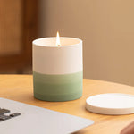 Bougie blanche et verte allumée posée sur un bureau en bois avec un papier à côté.