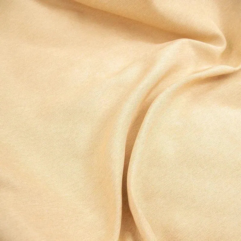 Texture douce d'un tissu beige plié, idéal pour la confection de vêtements et d'accessoires élégants. Cette étoffe offre une apparence naturelle et polyvalente, parfaite pour toutes les saisons.