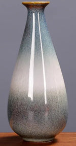 Vase céramique délicat aux nuances de gris et de blanc, avec une forme élancée et une texture irrégulière, reflétant un style artisanal.