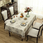 Une salle à manger élégante et accueillante, avec un buffet en bois sombre, une table recouverte d'une nappe ornée de motifs et une magnifique composition florale sur la table.