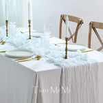 Une élégante table de fête avec des accessoires dorés, des assiettes blanches et une nappe blanche avec un motif texturé.