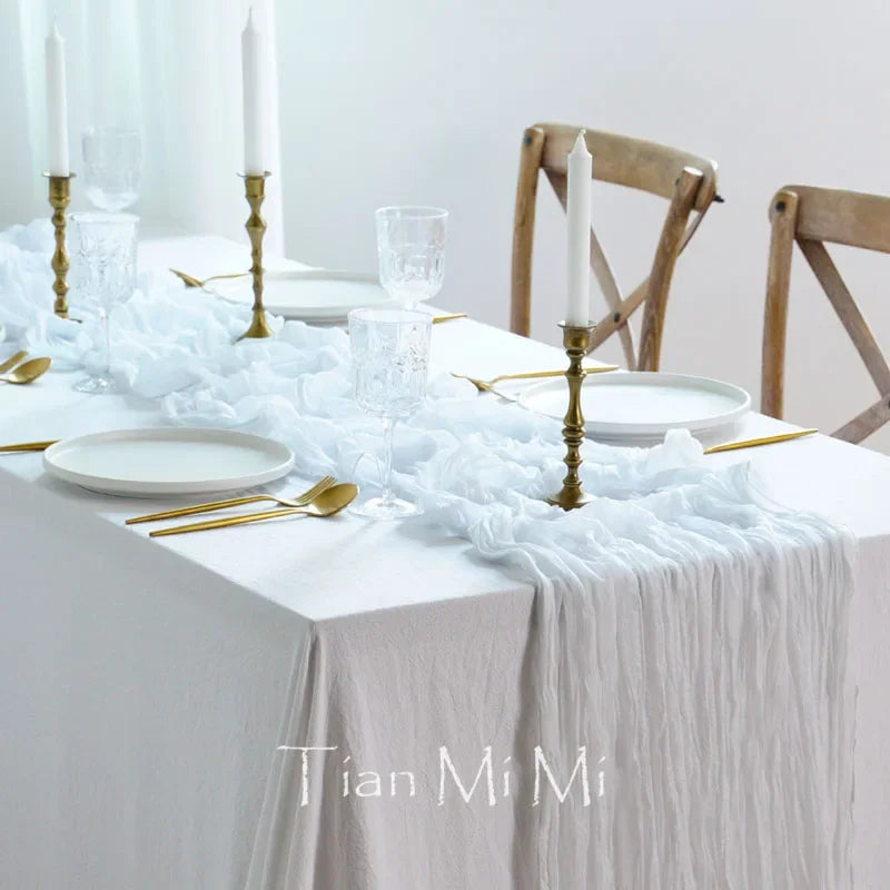 Une table de fête magnifiquement décorée, avec des chandelles dorées, des verres cristallins et une nappe blanche froissée, créant une ambiance élégante et raffinée.