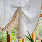 Rideau décoratif blanc avec motifs carrés, agrémenté de pompons élégants, attaché par un nœud délicat. Idéal pour ajouter une touche de charme à votre intérieur. Convient parfaitement pour une fenêtre de salon ou de chambre, apportant une ambiance lumineuse et aérée, tout en préservant l'intimité.