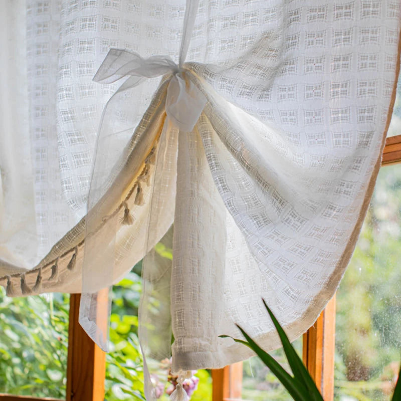 Rideau décoratif blanc avec motifs carrés, agrémenté de pompons élégants, attaché par un nœud délicat. Idéal pour ajouter une touche de charme à votre intérieur. Convient parfaitement pour une fenêtre de salon ou de chambre, apportant une ambiance lumineuse et aérée, tout en préservant l'intimité.