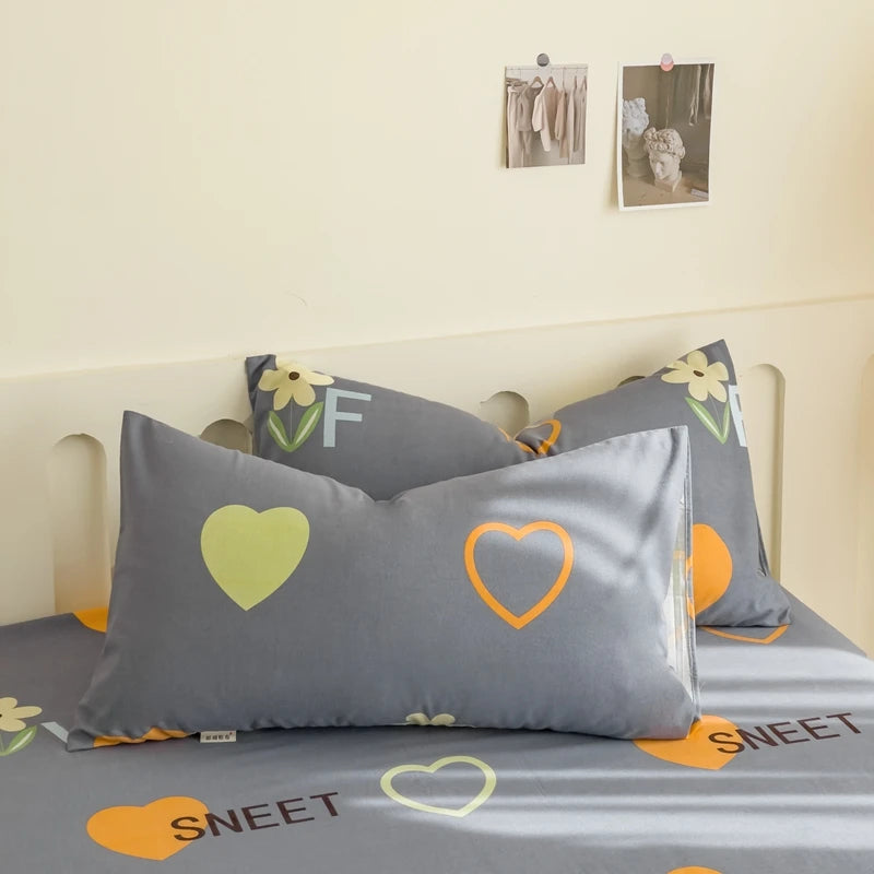 Coussin décoratif gris avec motifs de cœurs orange et verts disposé sur un lit avec des éléments décoratifs muraux.