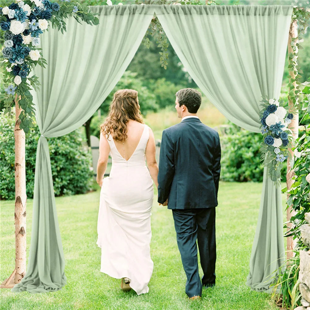 Un couple se tient la main et se dirige vers une arche de mariage ornée de fleurs verdoyantes dans un jardin luxuriant.