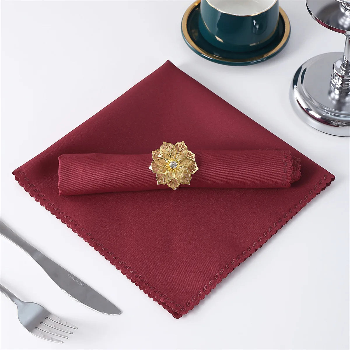 Un mouchoir de table rouge bordeaux avec une fleur décorative en or sur un fond de table blanche avec des ustensiles de table.