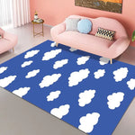 Tapis bleu marine avec nuages blancs stylisés, placé dans un salon moderne aux murs roses et avec un canapé rose.