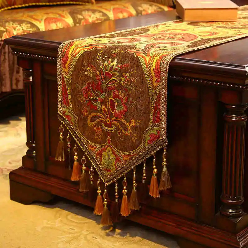 Un superbe chemin de table orné de motifs floraux colorés, aux couleurs chaudes et éclatantes, rehaussé de franges et de glands décoratifs.