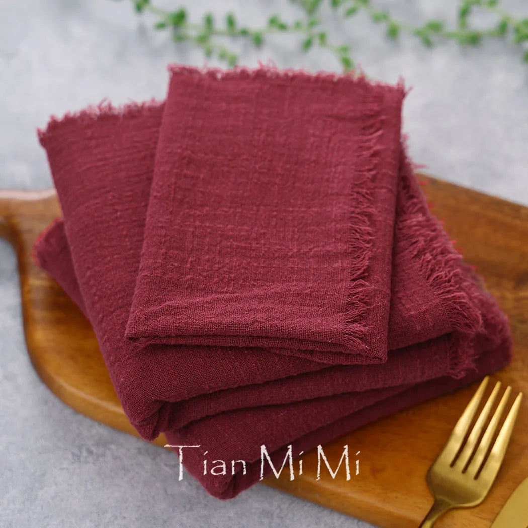 Serviettes bordeaux soigneusement pliées sur un plateau en bois avec des couverts, évoquant un service de table élégant.